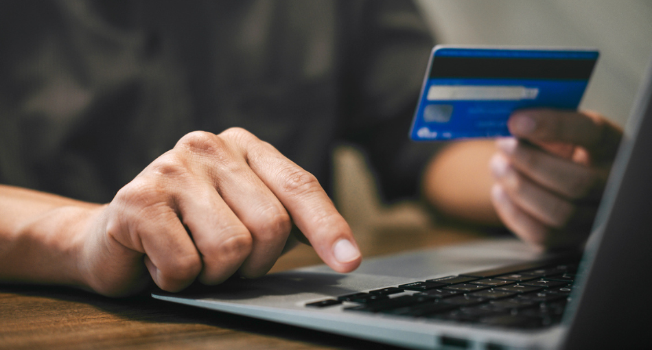 One hand typing information into a computer while the other holds a credit card.